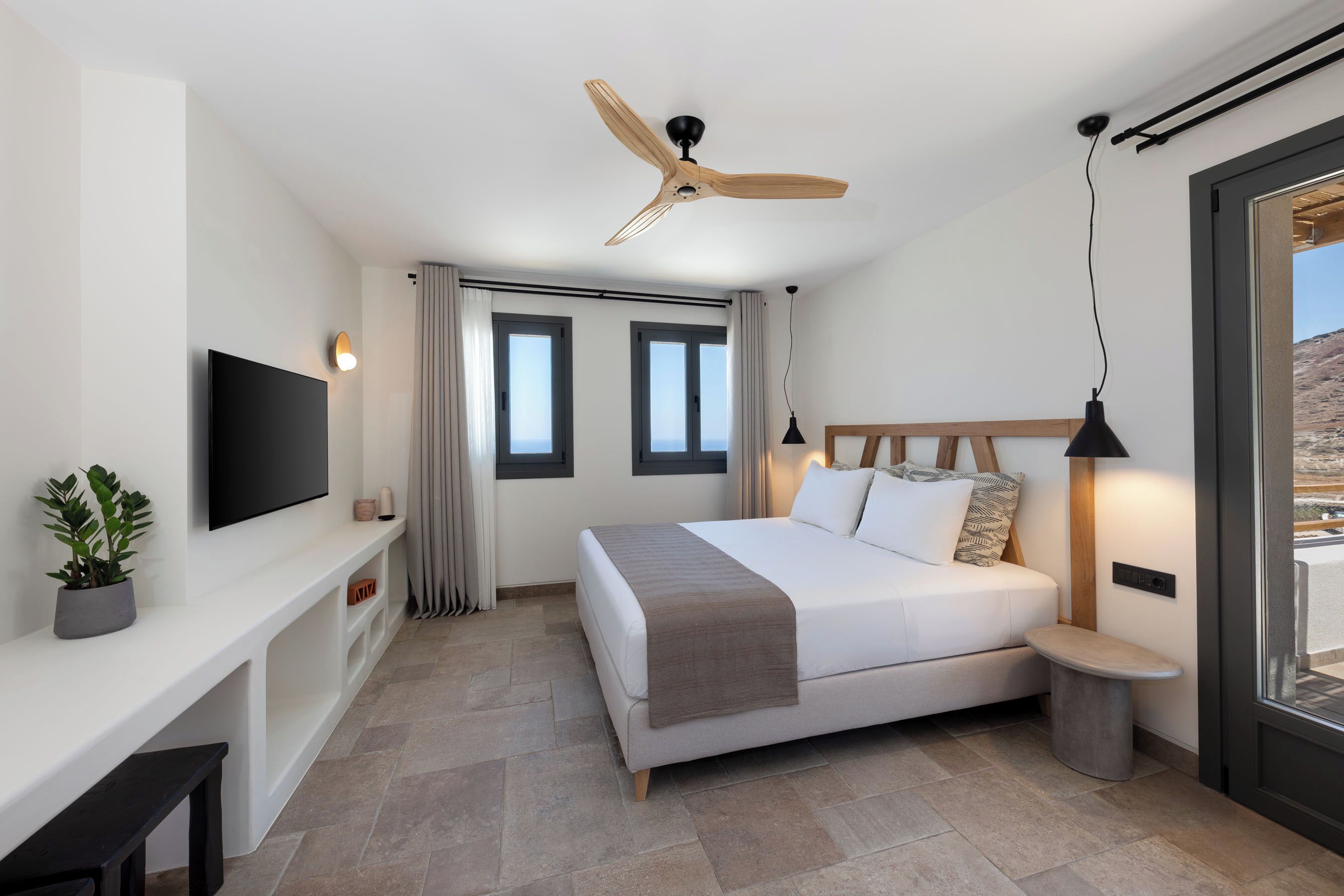 Een moderne slaapkamer met een bed, een televisie, een plafondventilator en een raam met gordijnen.