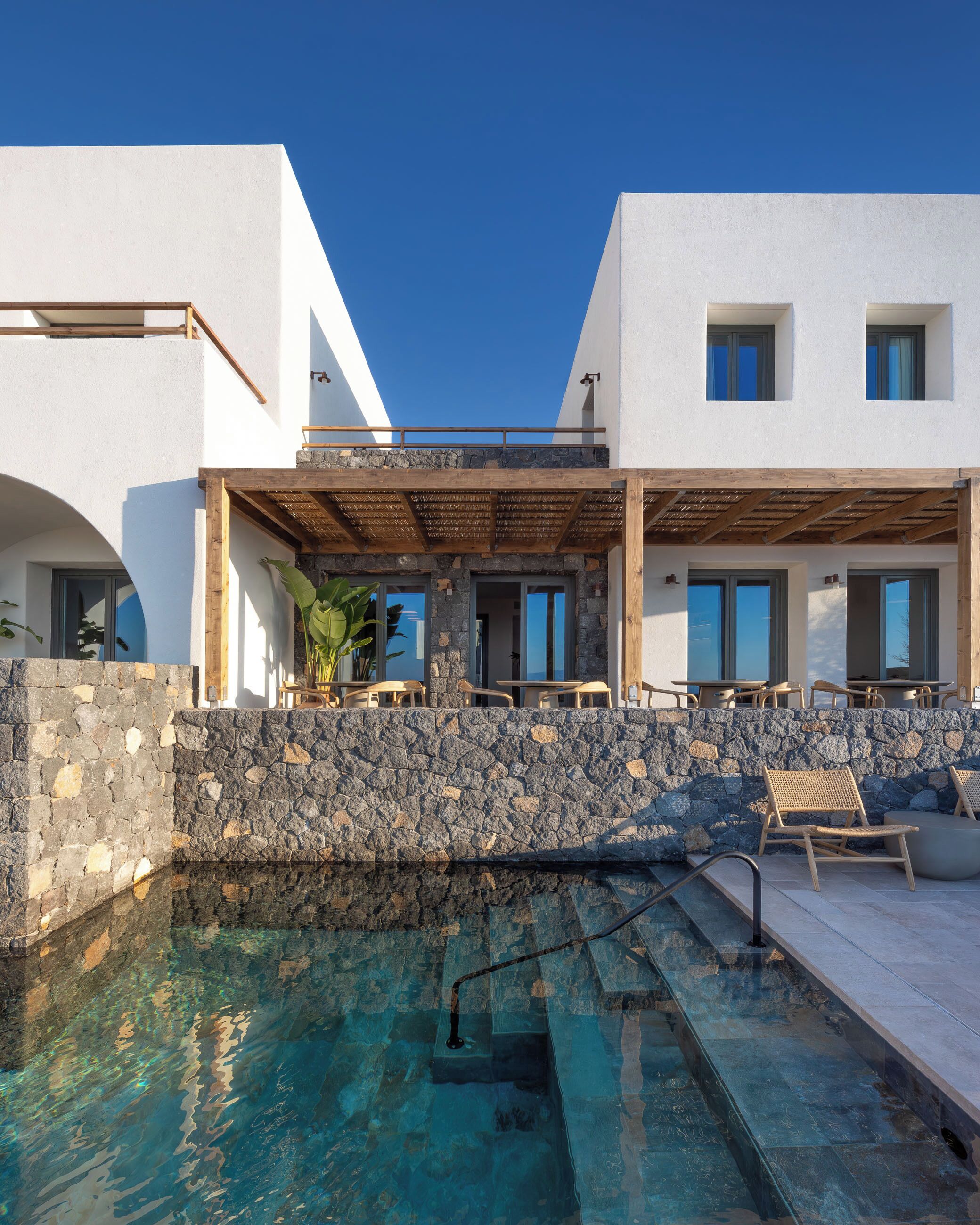 A modern building with a stone wall, a pool, and outdoor seating.
