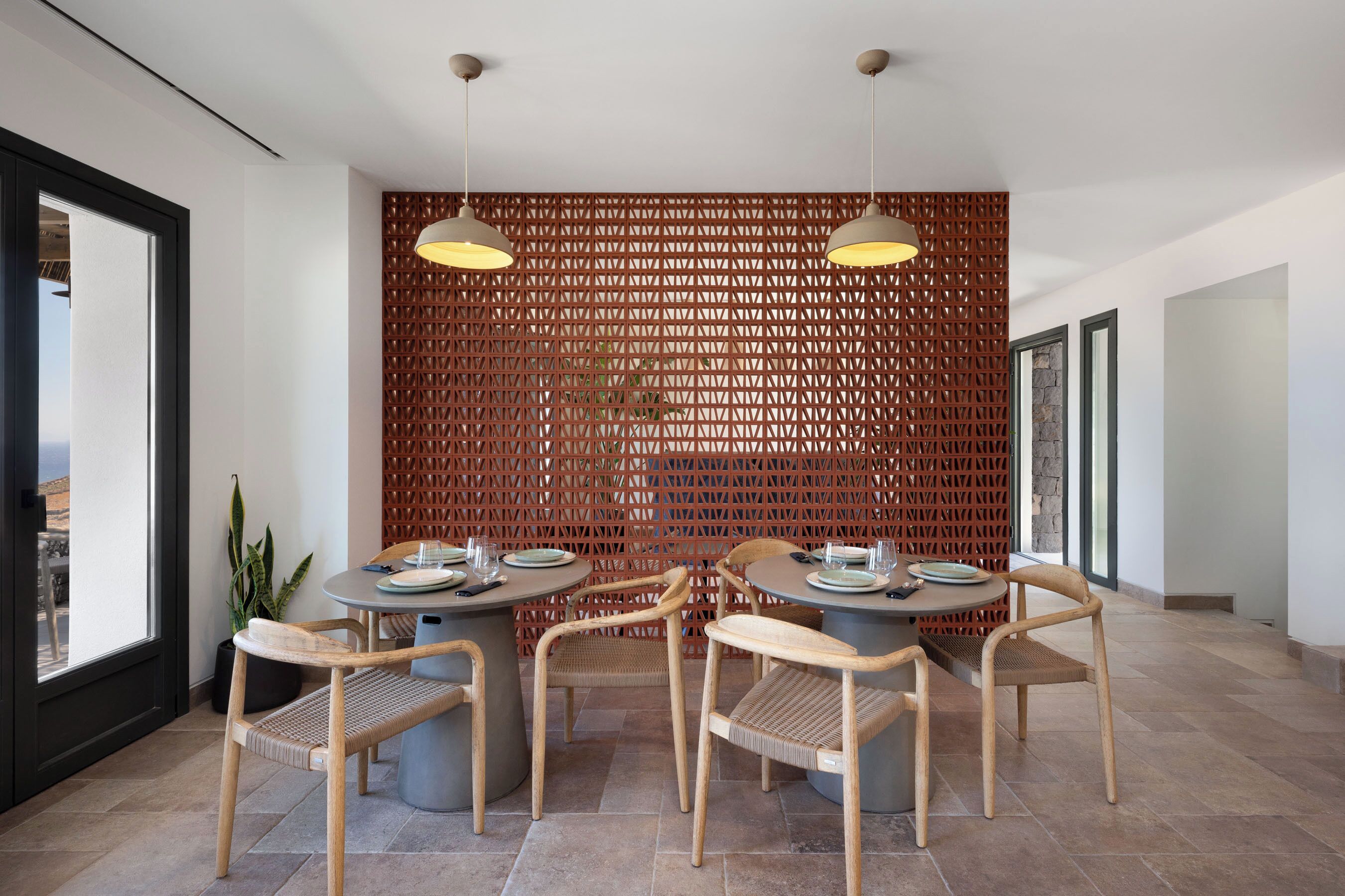 A dining area with round tables, wicker chairs, and pendant lighting.