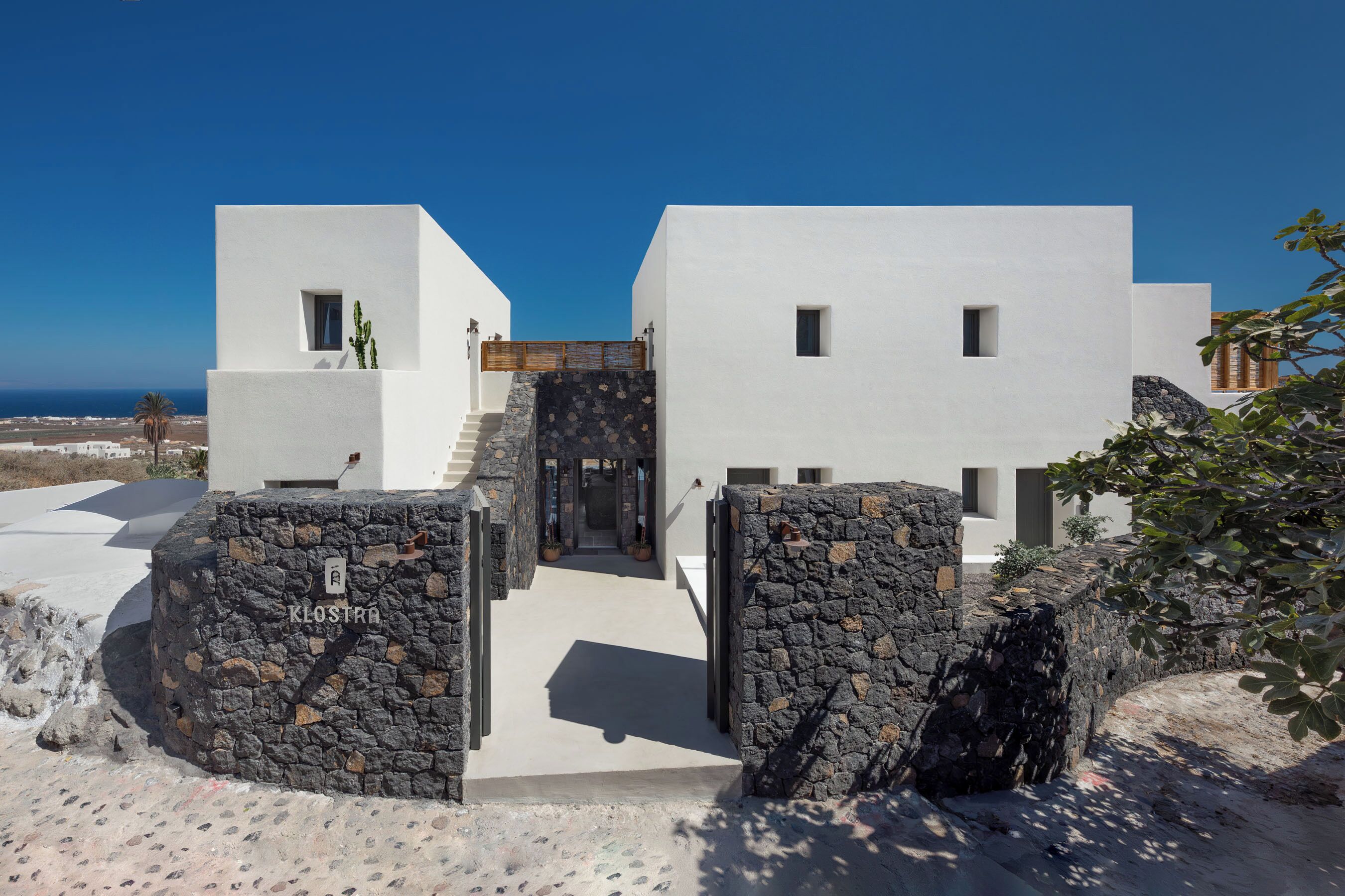 A modern building with a stone entrance, white walls, and a view of the sea.