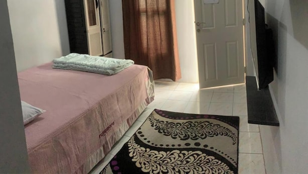 A small, well-lit room with a single bed, a wardrobe, a television, and a door leading to another room. - Hotel O Fgh Residence 1 (Bekasi)