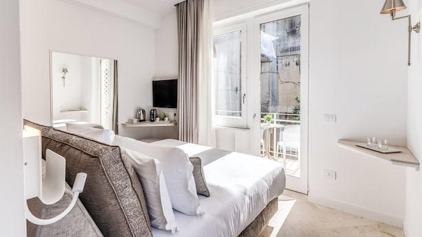 A modern hotel room with a large bed, a flat-screen TV, a bedside table, a mirror, and a balcony with a view of the city. - Diff'rent Souls Rooms (Sorrento)