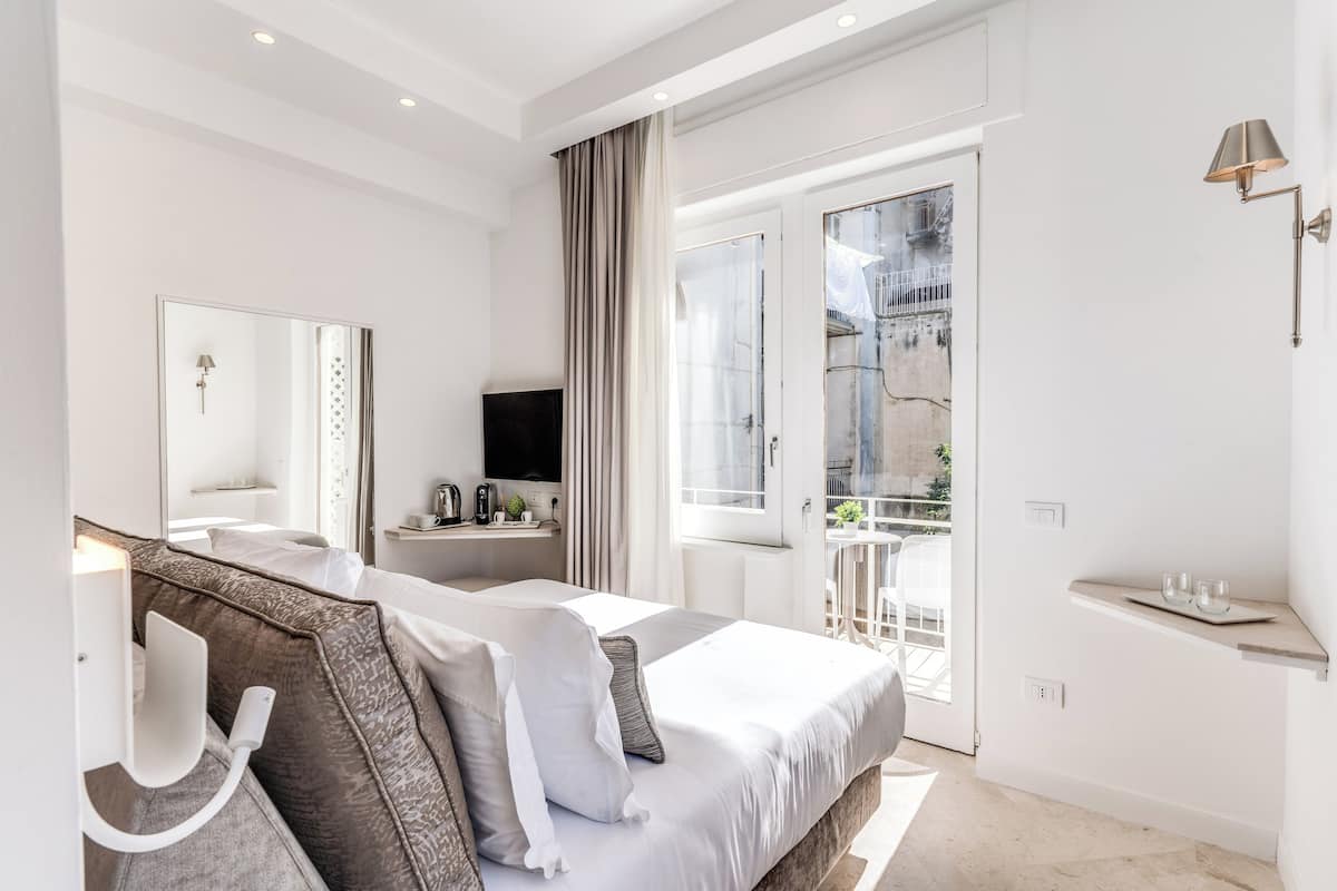 Una habitación de hotel moderna con una cama grande, un televisor de pantalla plana, una mesita de noche, un espejo y un balcón con vistas a la ciudad.