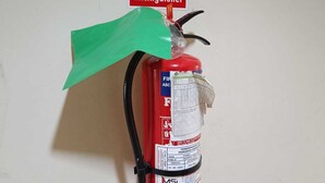 Un extintor colgado en la pared con un cartel verde que indica una ruta de evacuación.