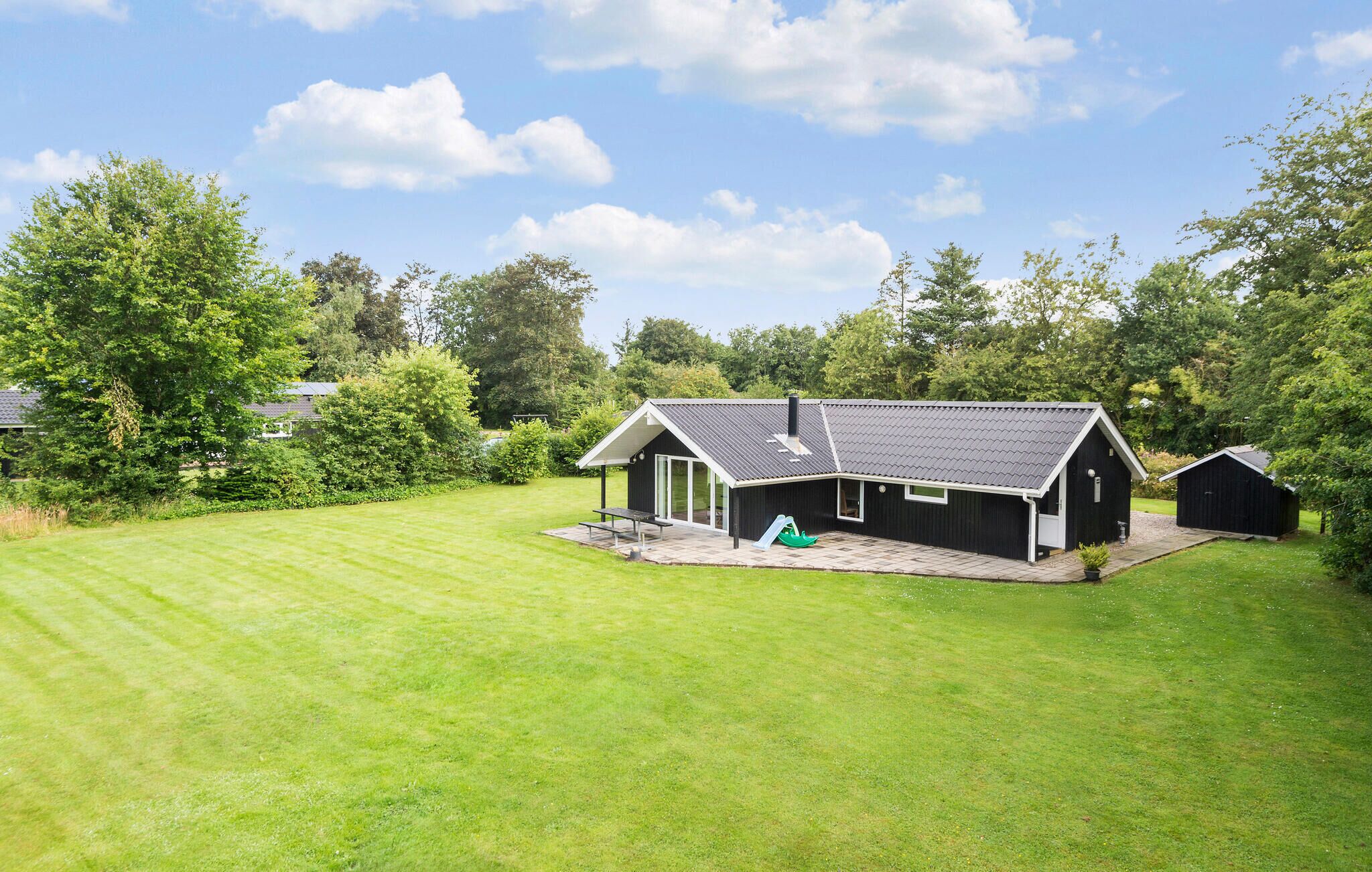 A modern house with a large lawn, a patio, and a green slide.