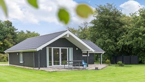 A modern building with a sloped roof and large glass doors, surrounded by a well-maintained lawn and trees. - 3 bedroom cozy home in Oksbøl (Oksbøl)