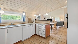 A modern kitchen with white cabinets, a dishwasher, and a coffee maker. There is a window with a view of greenery outside. - 3 bedroom cozy home in Oksbøl (Oksbøl)