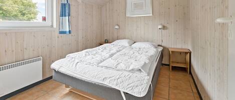 A bedroom with a bed, a window with curtains, a bedside lamp, a picture on the wall, and a small wooden table.