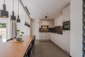 Et moderne køkken med hvide skabe, et træspisebord og hængende lamper.