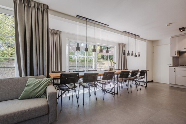A modern living room with a dining area, large windows, and a kitchen.