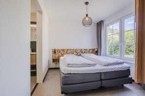 A bedroom with a bed, a nightstand, a wall-mounted lamp, and a window. - Family Escape With Garden (Bad Bentheim)