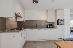 A modern kitchen with white cabinetry, a gas stove, a coffee maker, and a built-in oven.