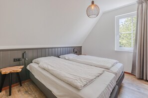 A bedroom with two beds, a wooden stool, a hanging light fixture, and a window with curtains.