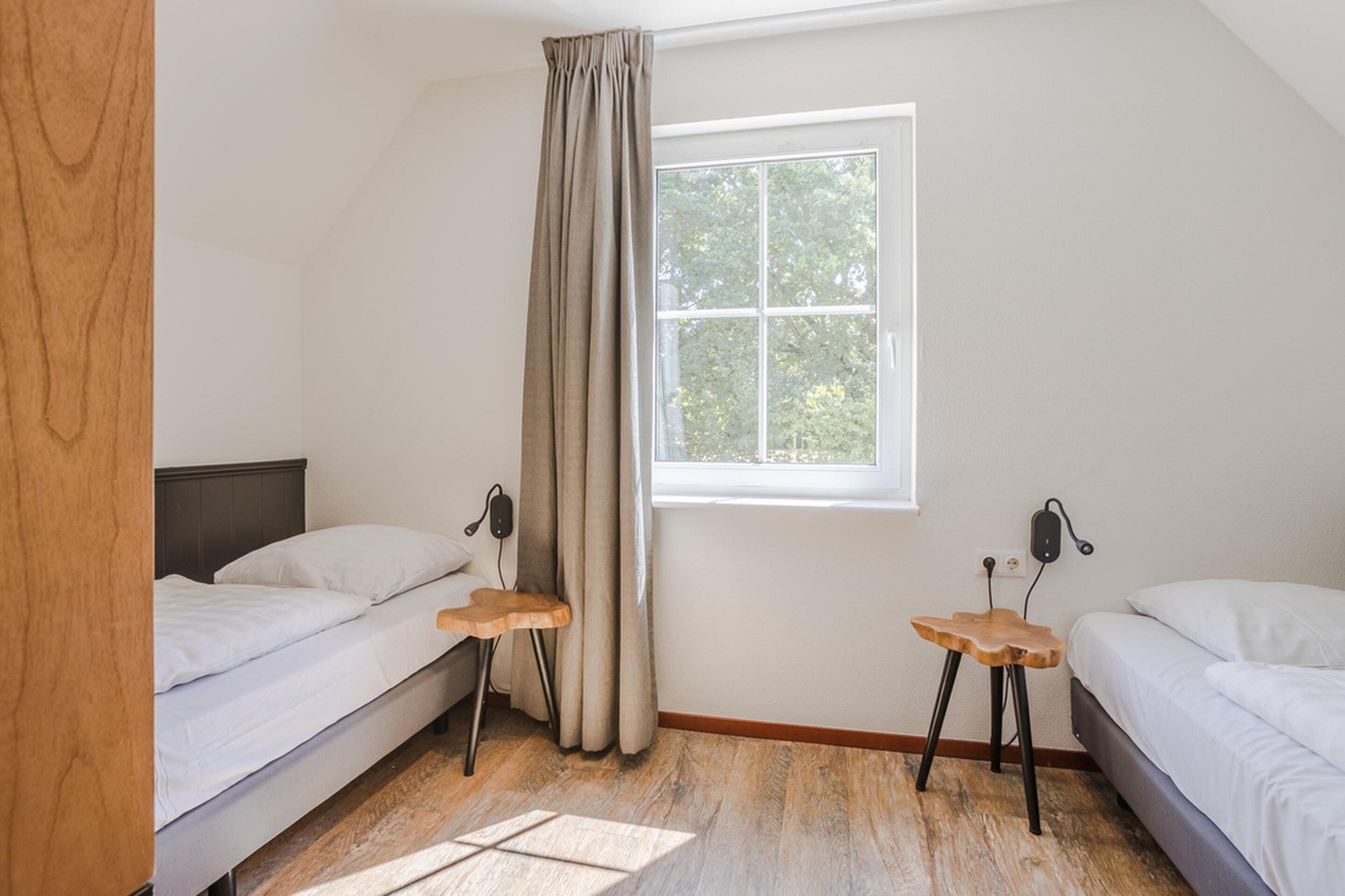 Un dormitorio con dos camas, una ventana con vistas a árboles y suelo de madera.