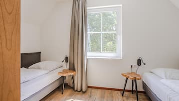 Un dormitorio con dos camas, una ventana con vistas a árboles y suelo de madera.
