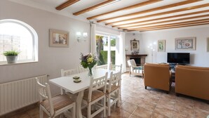 A dining area with a white table and chairs, a potted plant, and a vase of flowers. There is a television and a sofa in the background. - Frederic in Balc n del Mar (Javea)