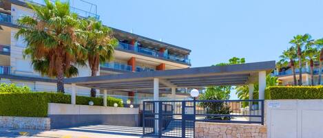 A modern hotel entrance with a covered walkway, palm trees, and a multi-story building with balconies.