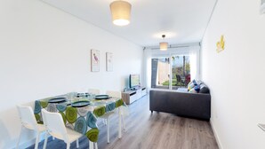 A modern dining area with a table set for four, white chairs, and a sofa in the background. - Happy in Oliva With 1 Bedrooms and 1 Bathrooms (Oliva)