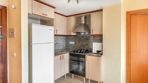 A compact kitchen with white cabinets, a stainless steel range hood, a built-in oven, and a white refrigerator. - Infante in Grau i Platja (Gandia)