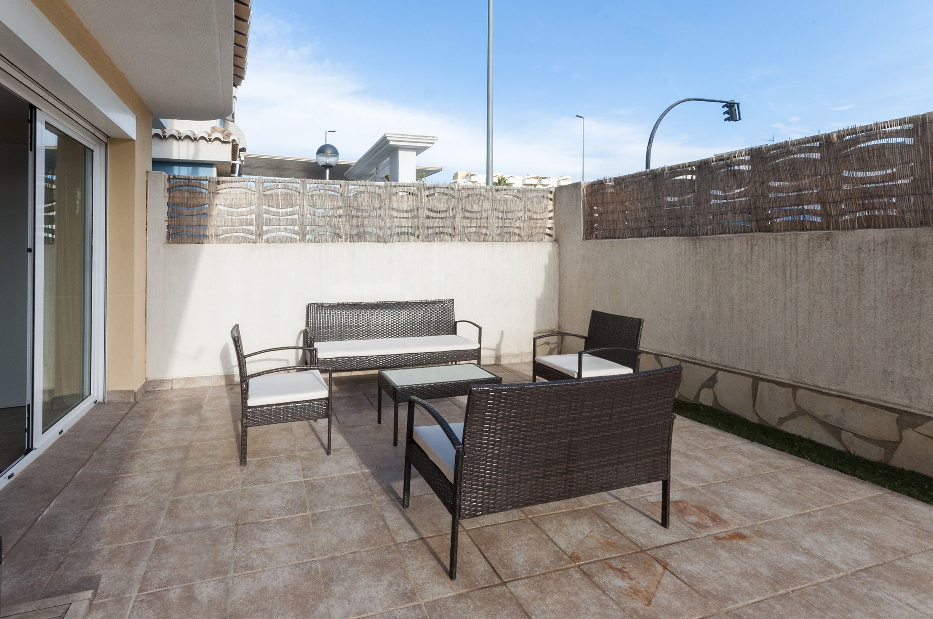 Un área de patio al aire libre con mobiliario de mimbre, piso de baldosas y pared de concreto.