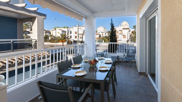 A sunlit outdoor dining area with a table set for four, surrounded by chairs, on a balcony with a railing. - Golden in Gandia With 3 Bedrooms and 3 Bathrooms (Gandia)