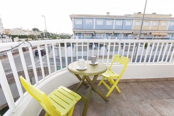 A balcony with yellow chairs and a table, overlooking a street with buildings and parked cars. - Golden in Gandia With 3 Bedrooms and 3 Bathrooms (Gandia)