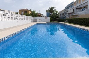 A swimming pool with clear blue water, surrounded by a white fence and a building with balconies.