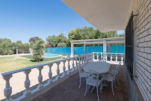 A patio with a white table and chairs, a pool, and a covered area with a white railing.