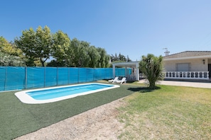 A swimming pool with a blue fence, a covered patio area, and a house in the background.