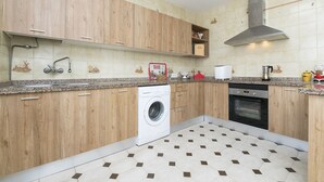A kitchen with wooden cabinets, a washing machine, an oven, and a tiled backsplash. - Fuentes Del Colorao in Barrio Nuevo (Conil de la Frontera)
