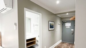 Een gang met houten vloer, een deur met een bordje, en een badkamer die zichtbaar is door een open deur.
