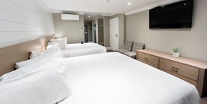 Two large beds with white linens and a TV are featured in this stylish room.