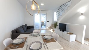 Un comedor moderno con una mesa preparada para cuatro personas, un sofá, un televisor y una escalera.