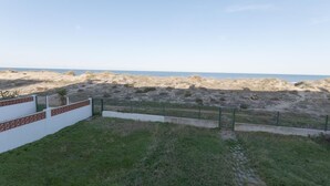 Una playa arenosa con cielo despejado, una pared blanca con tejas rojas y una cerca verde.