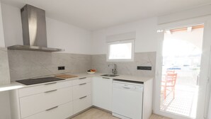 Una cocina moderna con armarios blancos, una campana de acero inoxidable, un lavavajillas y un ventanal que proporciona luz natural.