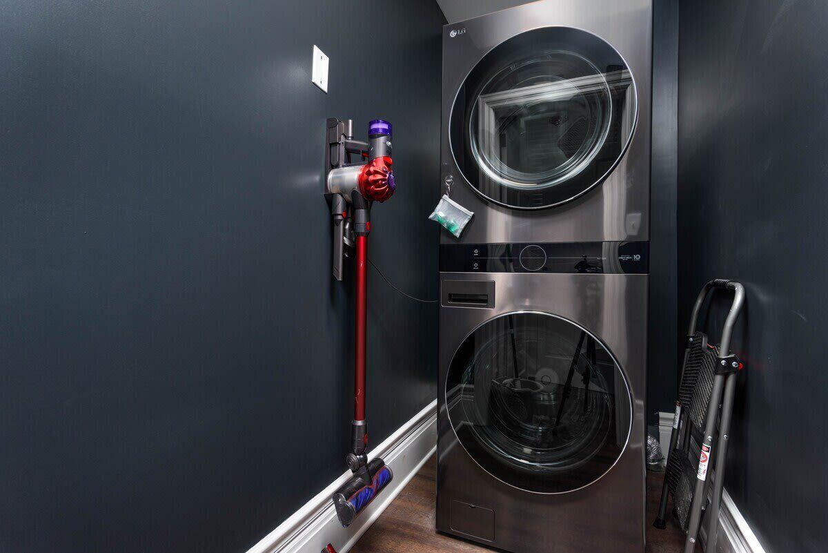 Une buanderie moderne équipée de deux machines à laver à chargement frontal en acier inoxydable, d’un tuyau rouge et d’une chaise pliante noire.
