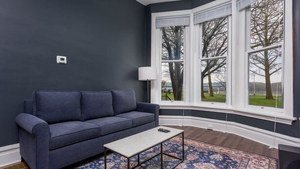 Un canapé bleu foncé, une petite table et un tapis à motifs dans une pièce aux murs sombres et aux grandes fenêtres.
