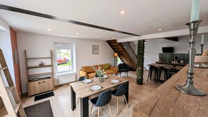 A spacious living area with a wooden dining table set for four, a sofa, and a staircase leading to an upper level. - Maison Lac et Jardin (Mesnil-Saint-Père)