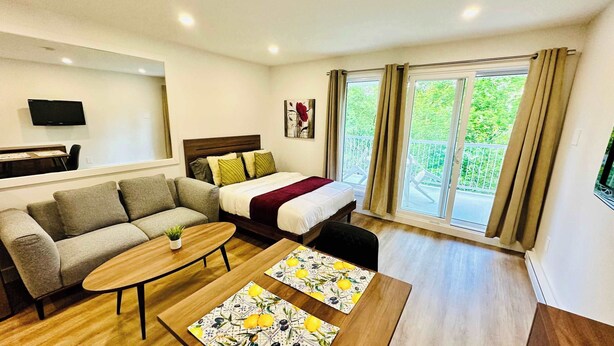A modern hotel room with a sofa, a bed, a small table, and a balcony with curtains. - Swimming Pool & Spa | Condo Mont Tremblant 2 (Mont-Tremblant)