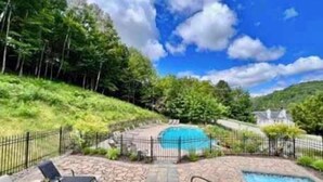 A pool area with a stone patio, lounge chairs, and a fenced perimeter. - Swimming Pool & Spa | Condo Mont Tremblant 2 (Mont-Tremblant)