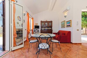 Ein Essbereich mit einem runden Tisch, vier Stühlen, einem roten Sofa, einem Schrank mit Glastüren und einem Fernseher.