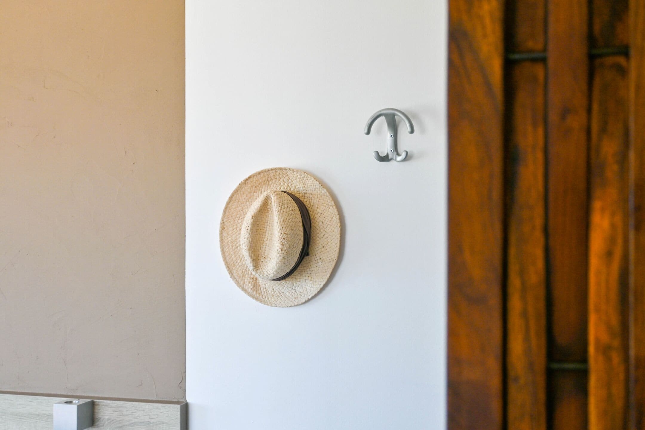 A hat hanging on a wall with a metal hook and a wooden door in the background.