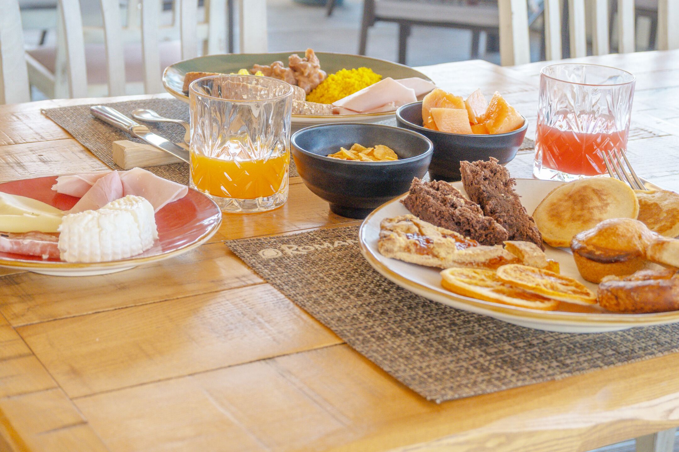 Et morgenbord rigt med flere retter, herunder æg, kød og frugt, samt to glas juice.