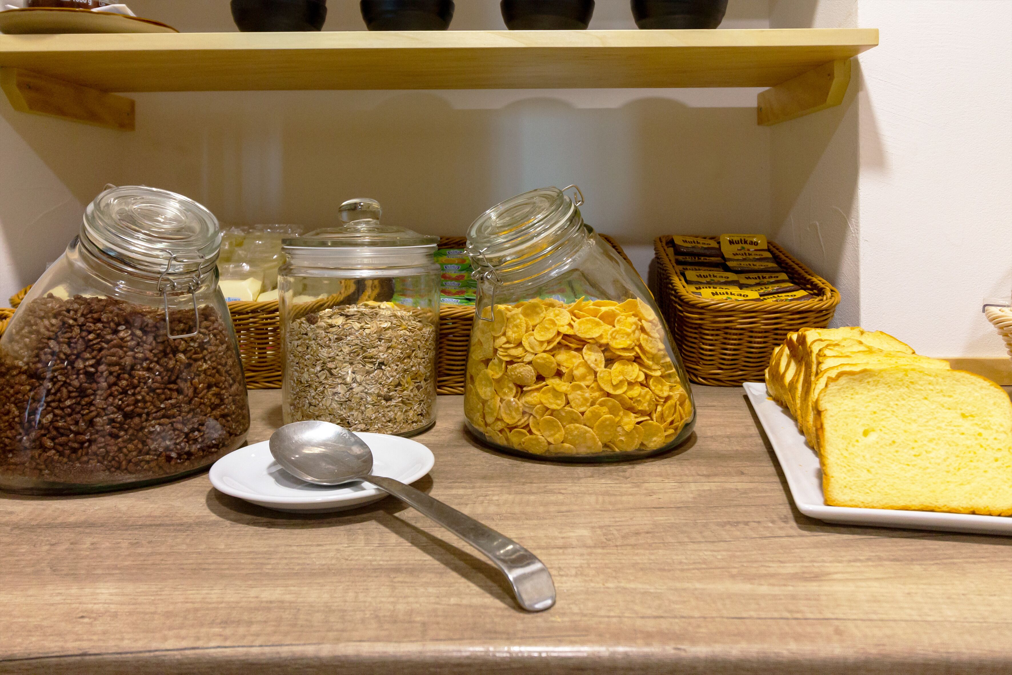 Un bufé de desayuno con diferentes alimentos, incluyendo cereales, pan y una cuchara sobre una mesa de madera.