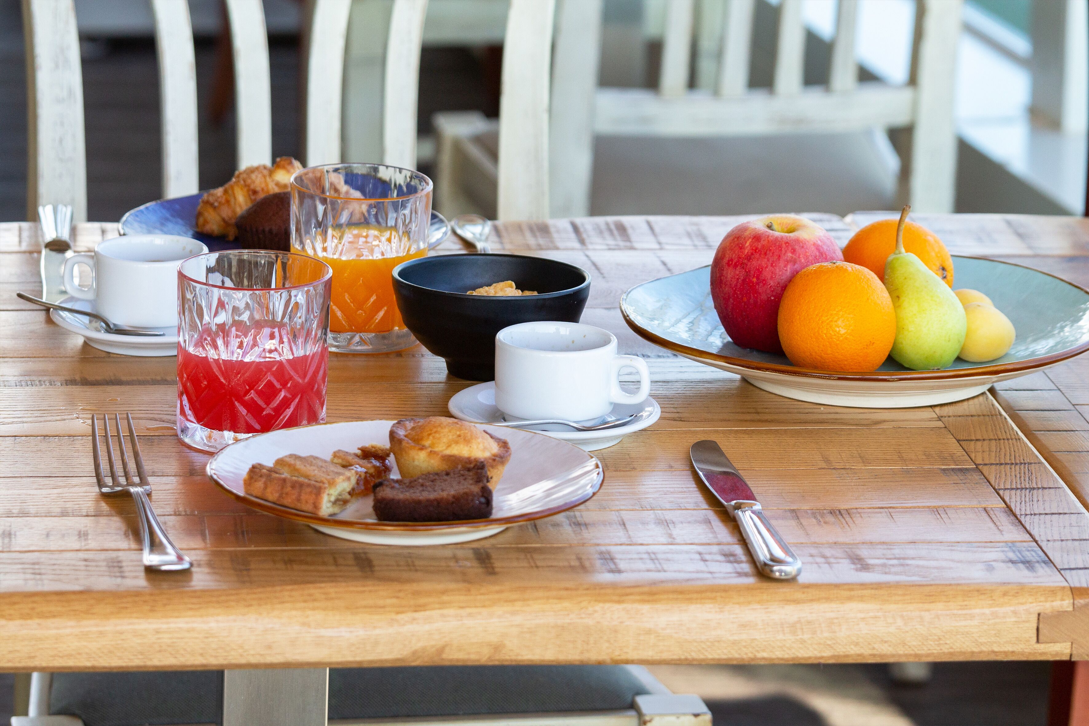 Ein Frühstückstisch mit Croissants, Muffins, Orangensaft und Obst.