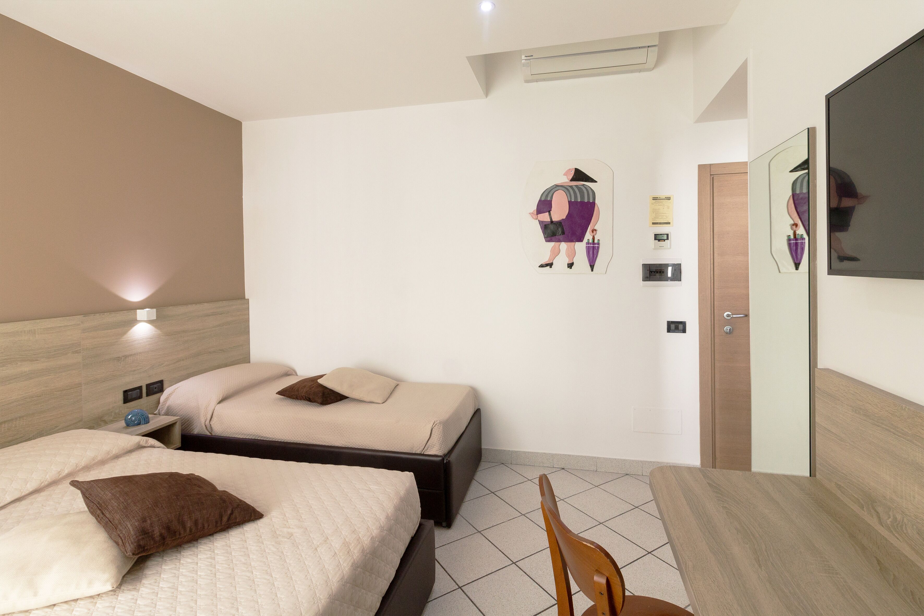 A hotel room with two beds, a wooden headboard, a mirror, and a small table.