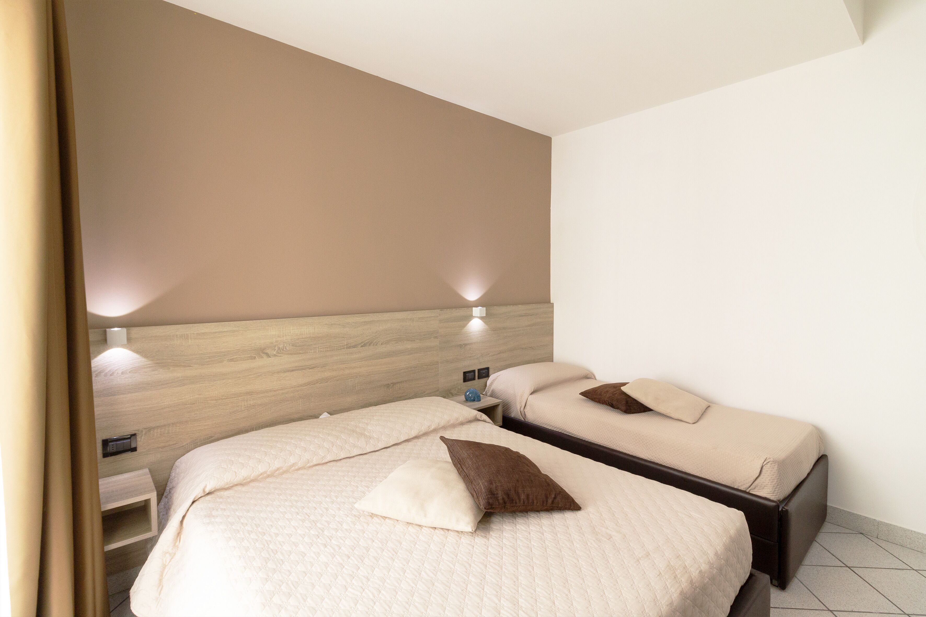 A hotel room with two beds, each with a pillow and a bedside table.