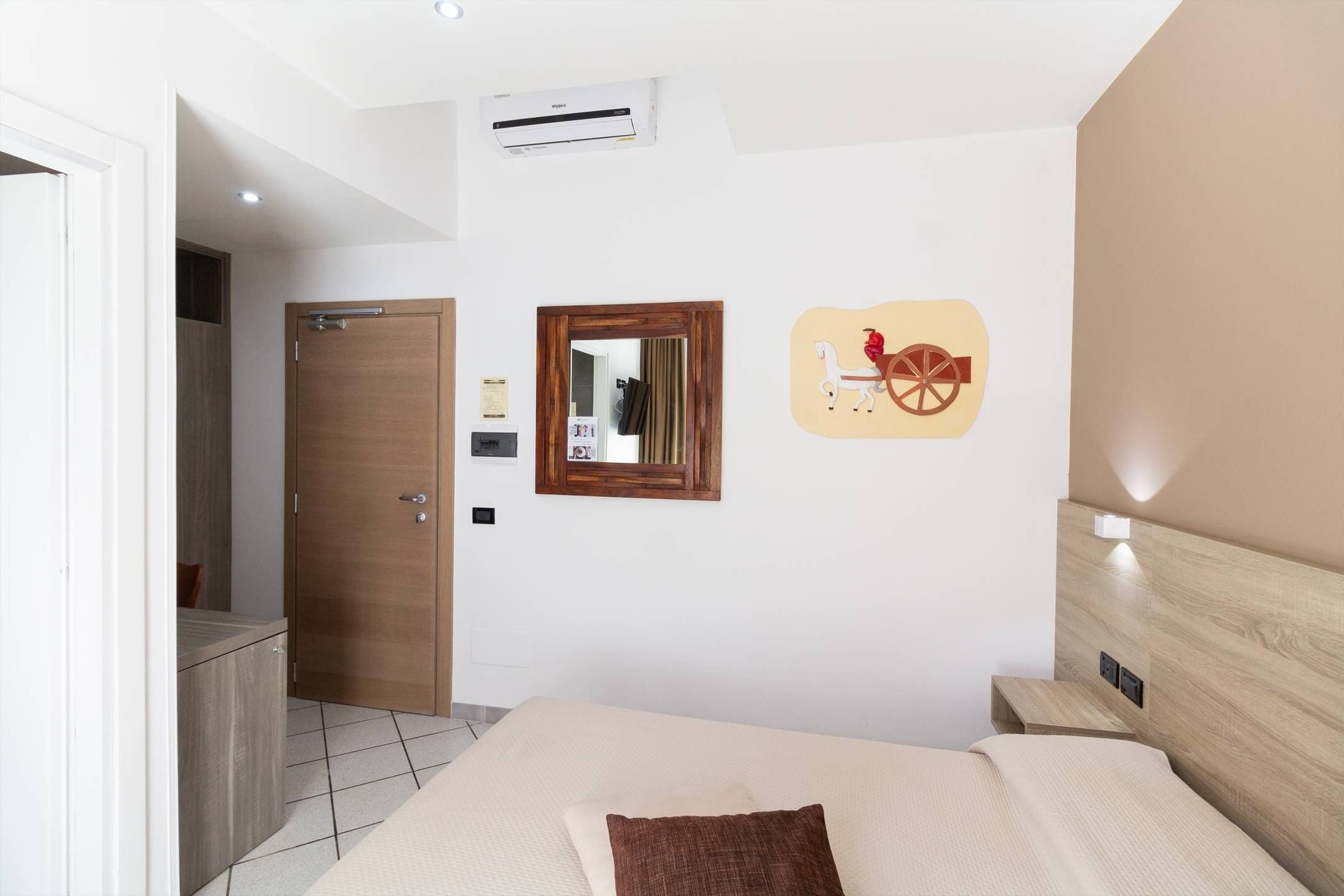 Una camera d'albergo con un letto, una testiera in legno, uno specchio fissato alla parete e un elemento decorativo a parete.