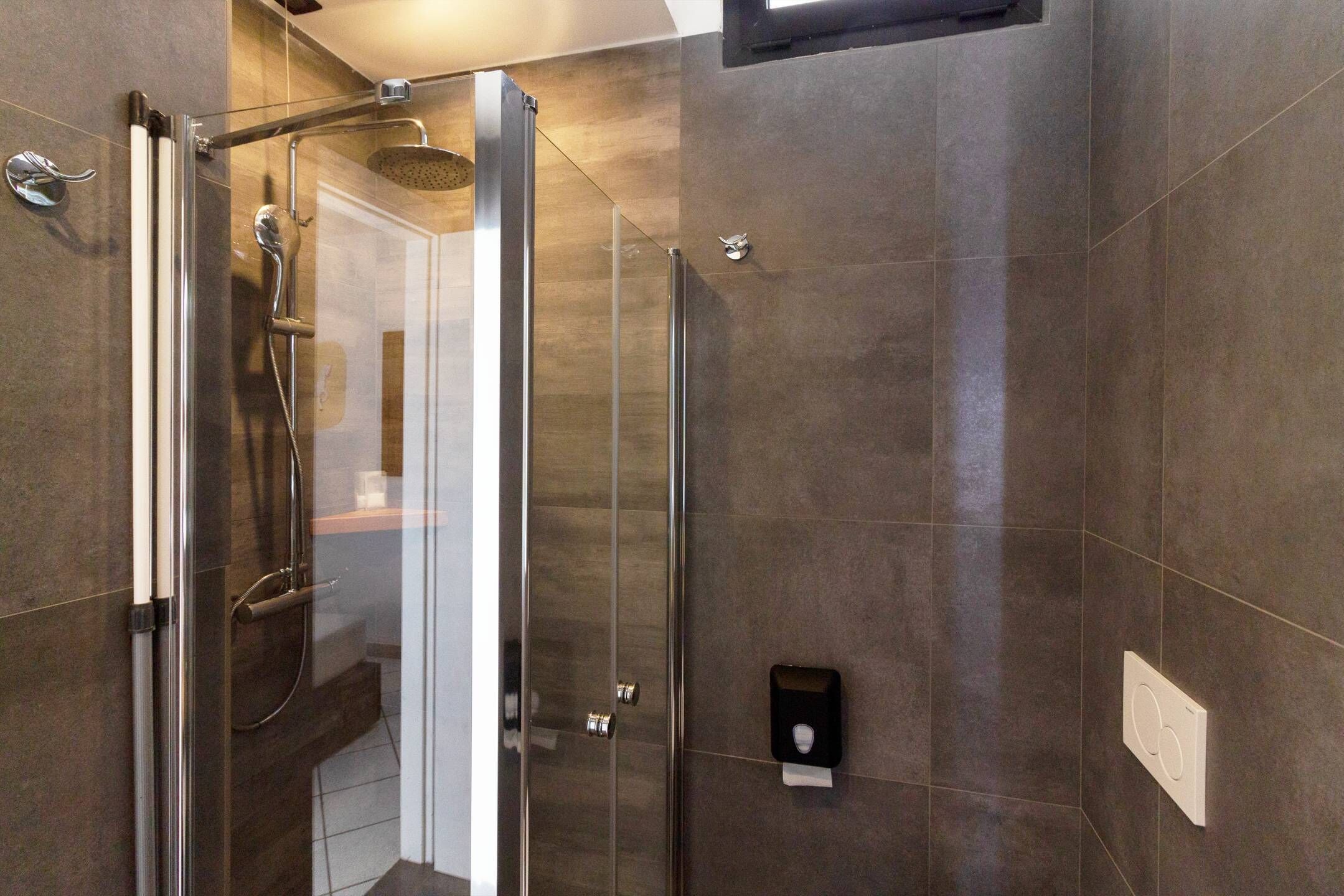 Un baño moderno con cabina de ducha de vidrio, ducha de mano y dispensador de toallas en la pared.
