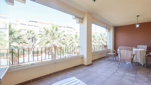 Un balcon offrant une vue sur les palmiers et les immeubles, avec des chaises en osier et une table.
